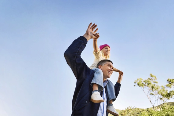 Happy parent with child on shoulders under clear sky
